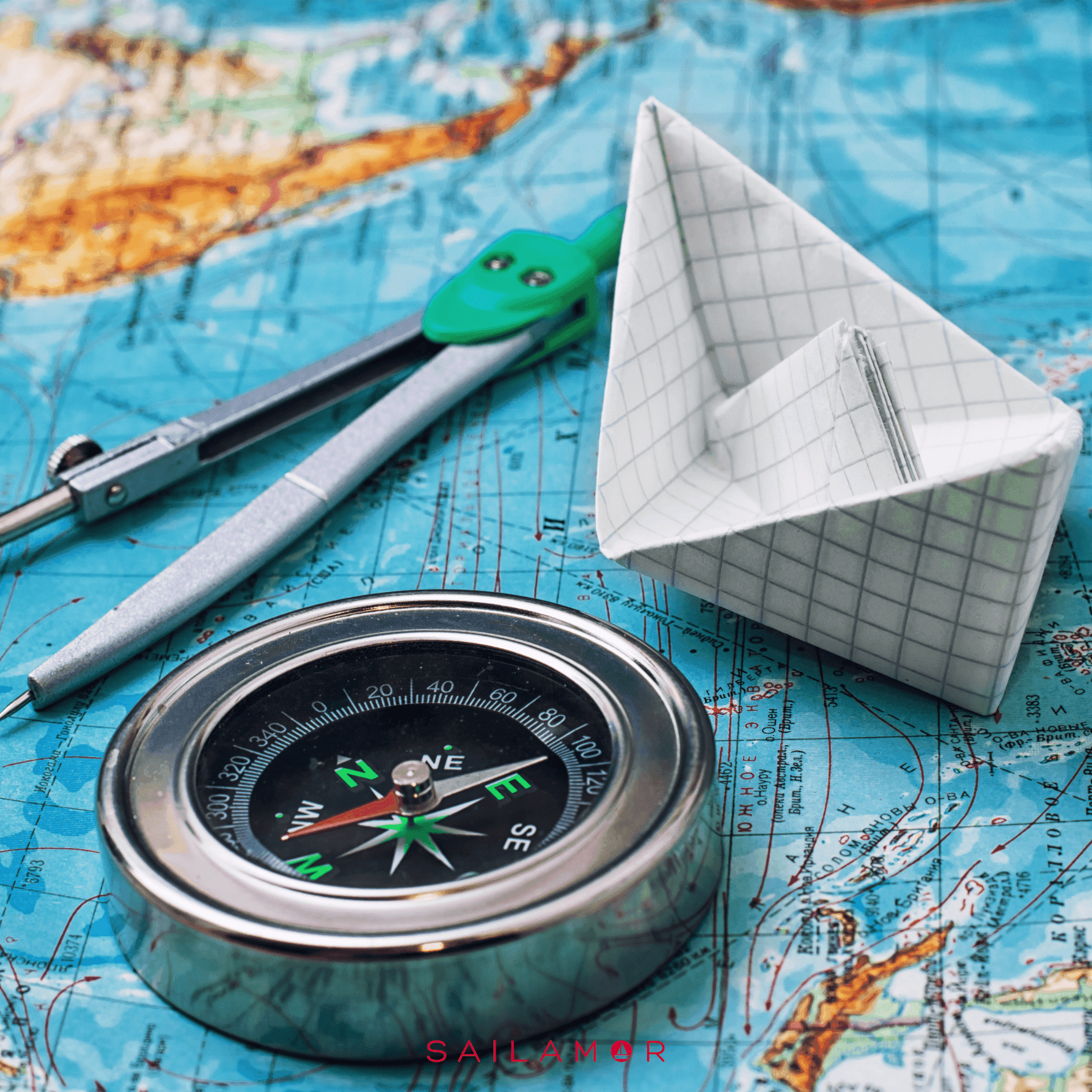 Compass, drawing compass, and origami paper boat on a blue nautical map.