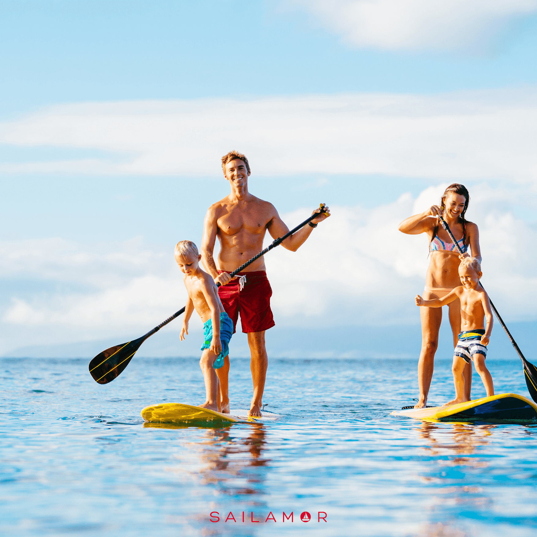 Two adults and two children enjoying paddleboarding on calm ocean waters under a clear blue sky.