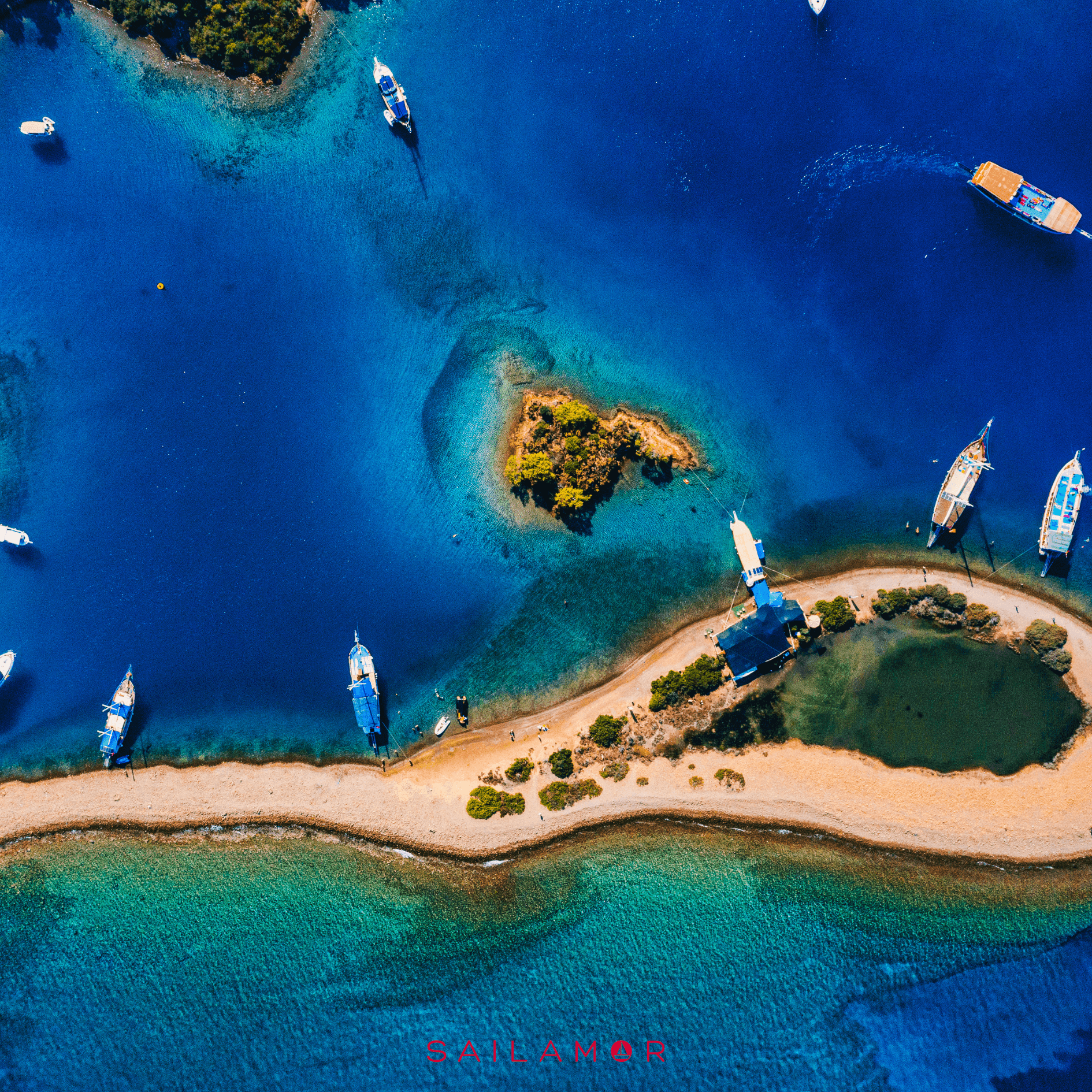 Aerial view of boats anchored near a small island with clear blue water and sandy beaches.