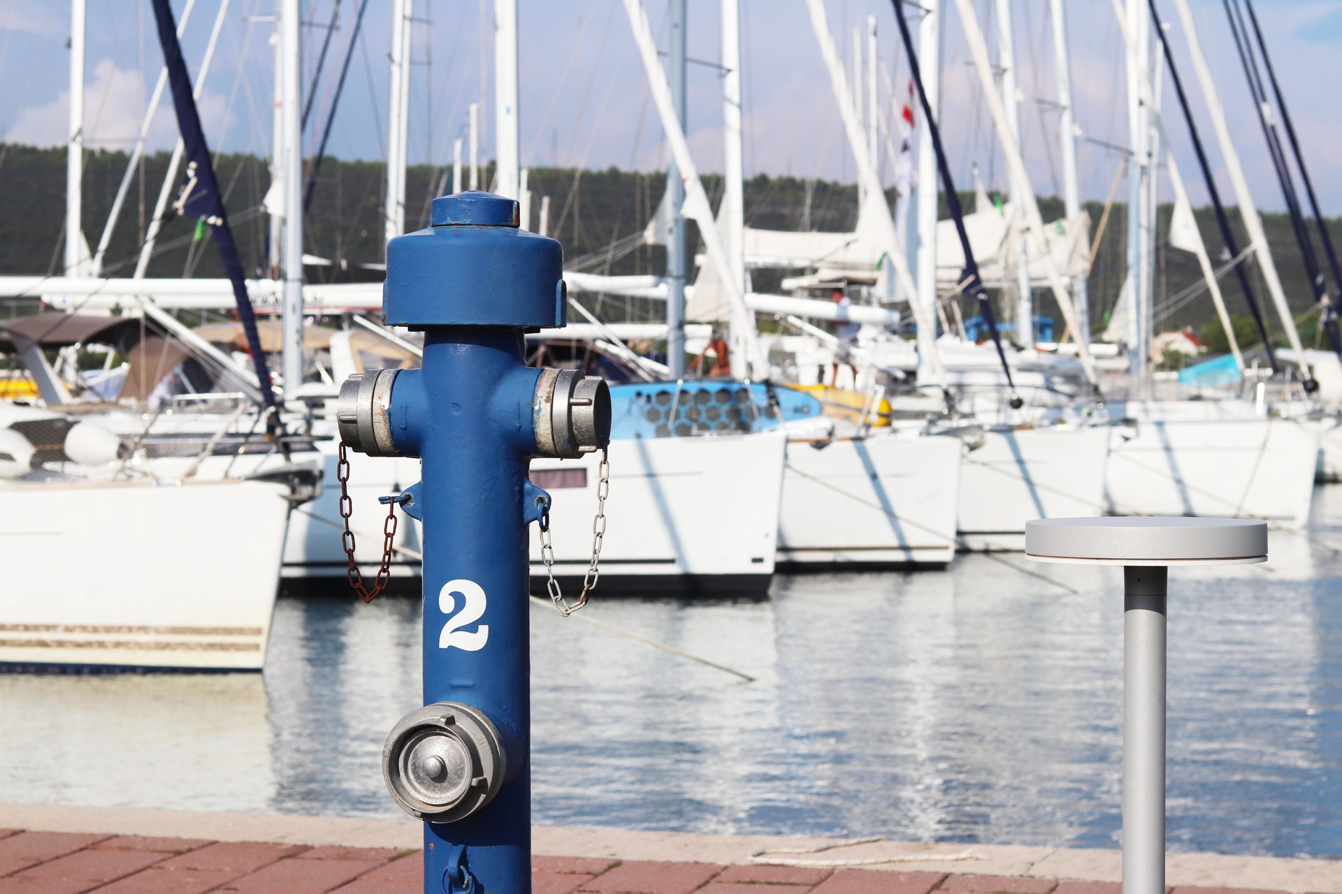 Hydraulic fire-fighting crane of blue color on the quay of the marina against the background of the parked sailing yachts. Fire safety of the port and carbon charter boats. Fighting the elements